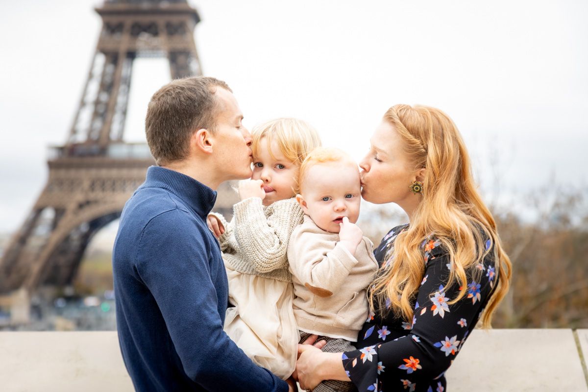 A family shares a tender moment together in front of the Eiffel Tower in Paris on a cloudy winter day.