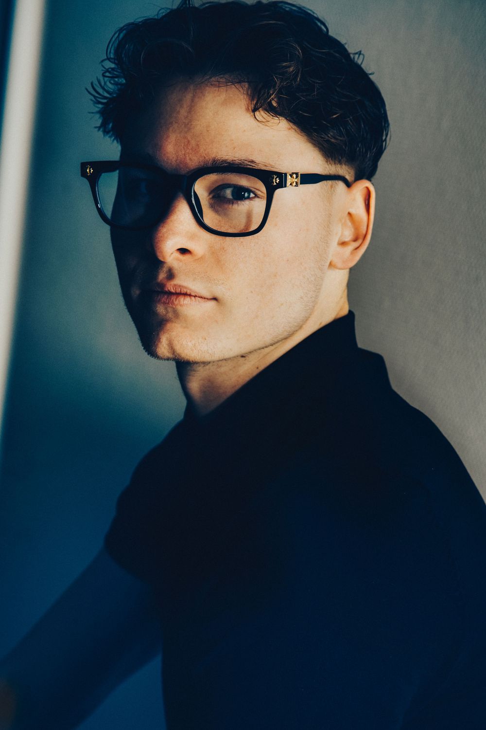 Artistic portrait series showing dramatic angles and shadows of a person wearing glasses against a dark blue background.