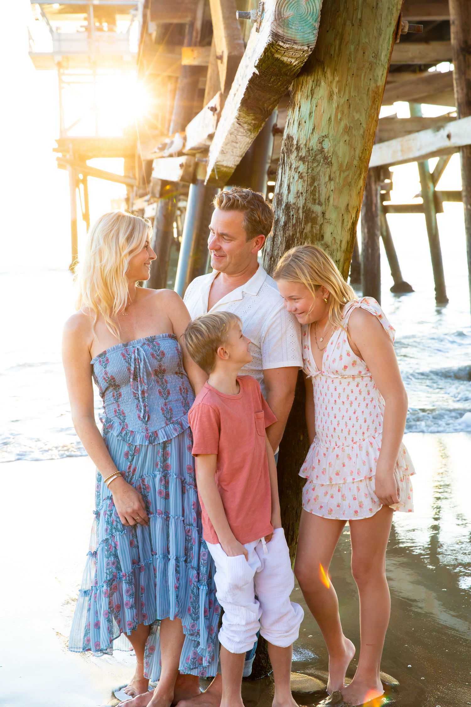 Family enjoying a sunny afternoon under a pier at the beach with golden sunlight streaming through the wooden posts.