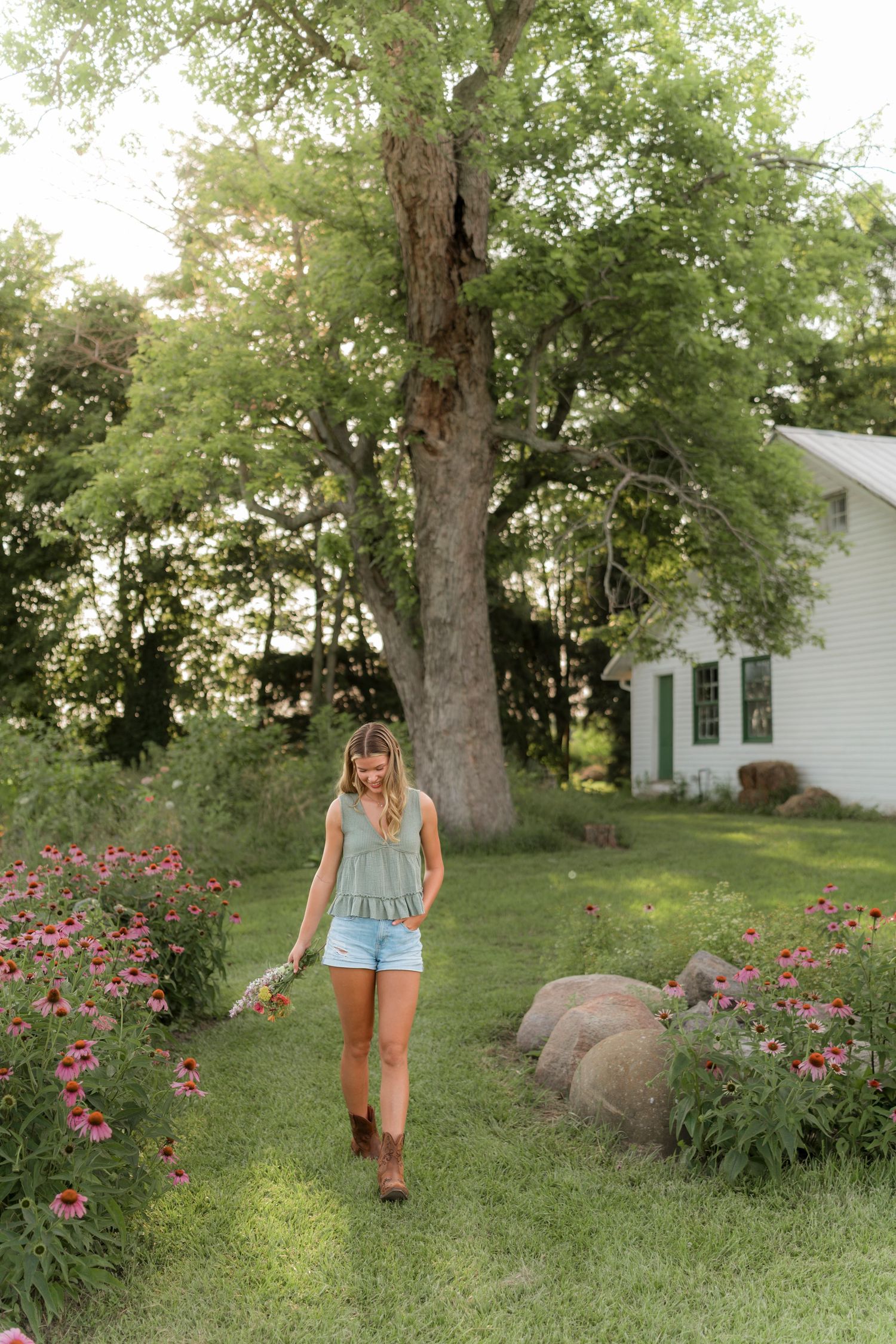 A person in a turquoise dress poses in a sunny field with wildflowers during golden hour.