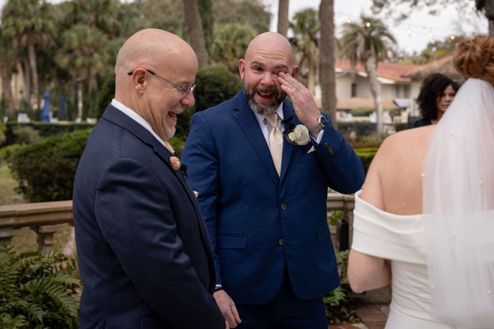 Wedding guests gathered outdoors under palm trees during a daytime celebration.