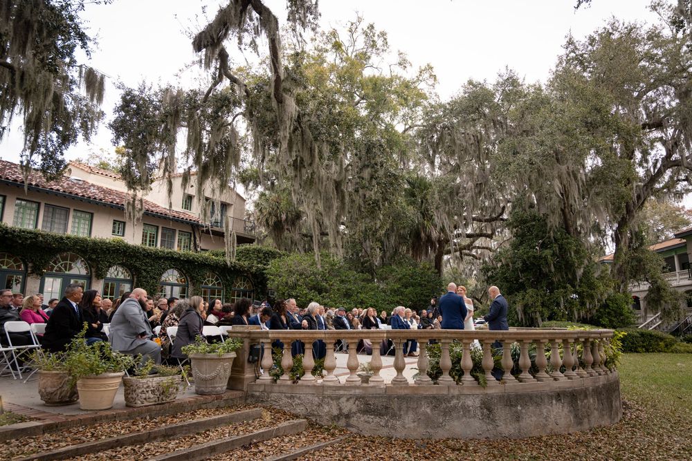 Historic stone balustrade walkway surrounded by Spanish moss-draped oak trees in a Southern garden setting.