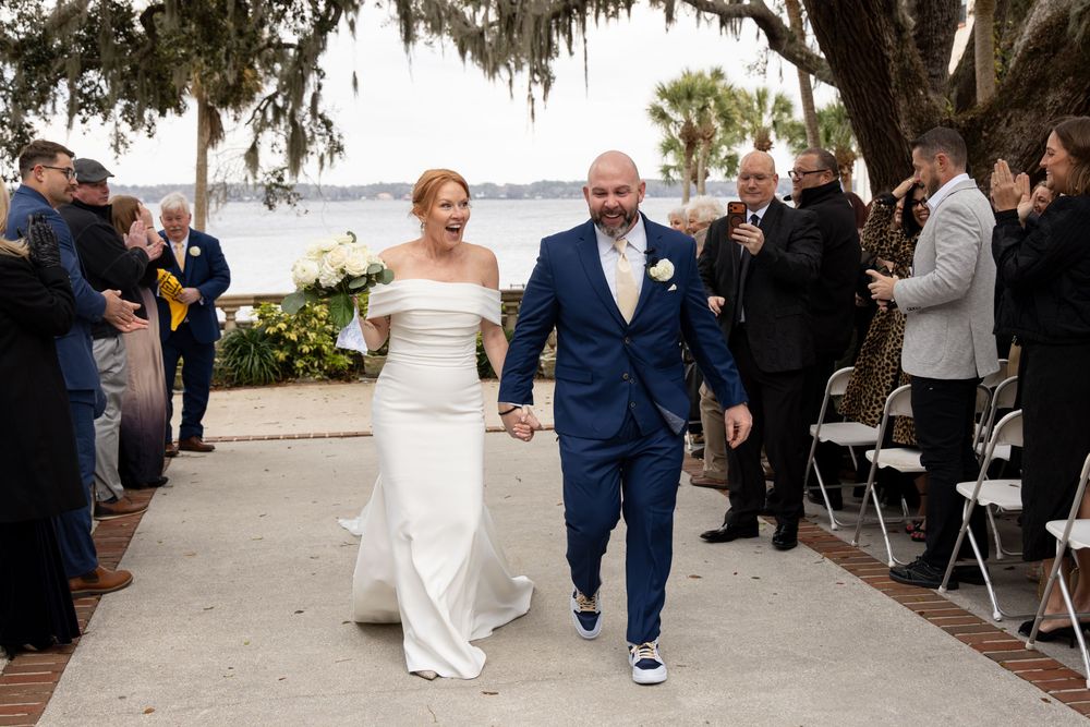 Wedding ceremony exit along waterfront pathway with guests looking on.