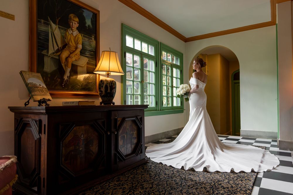 A bride in a flowing white wedding gown stands gracefully in a sunlit hallway with elegant interior decor.