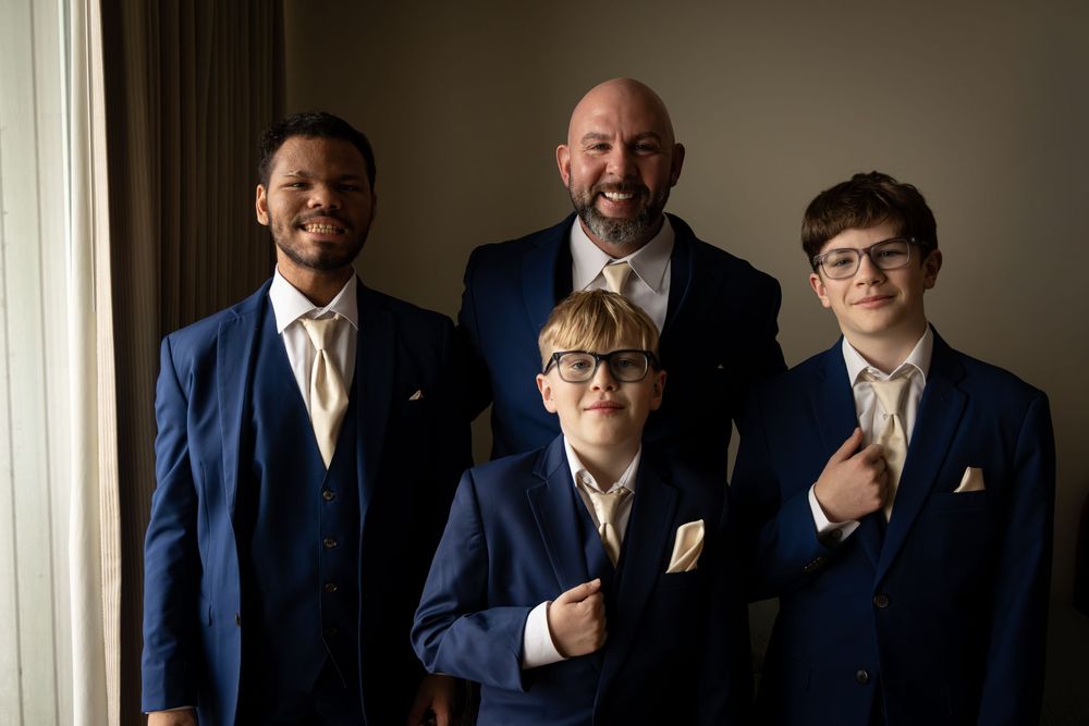 A group of people in navy blue suits stand together for a formal photograph against a light colored wall.