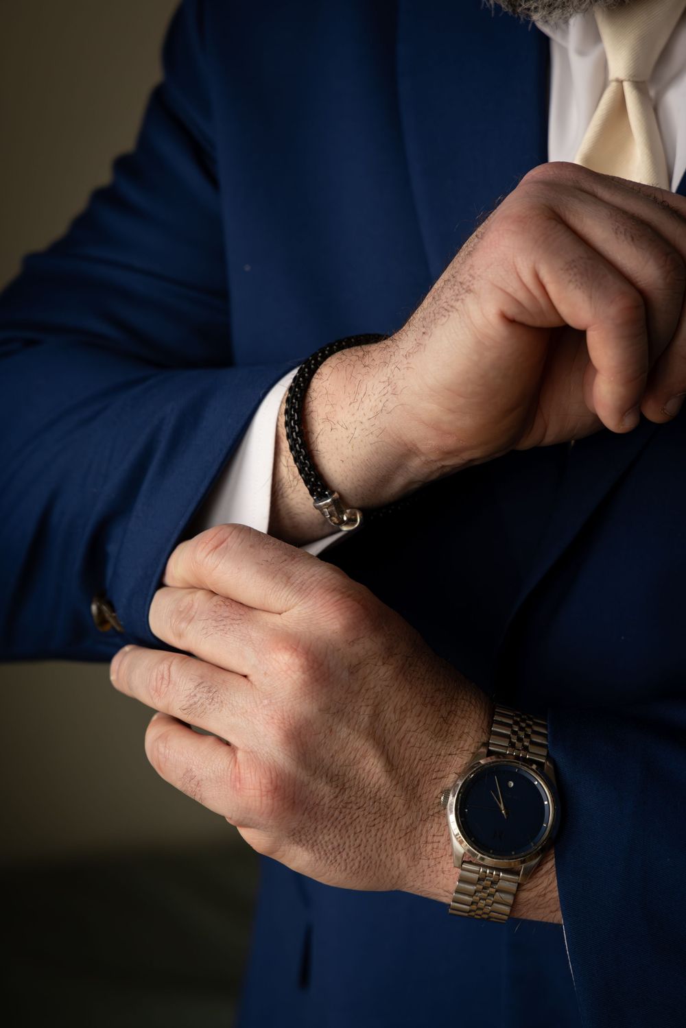 Close-up of hands adjusting shirt cuffs wearing a navy suit jacket and silver watch.