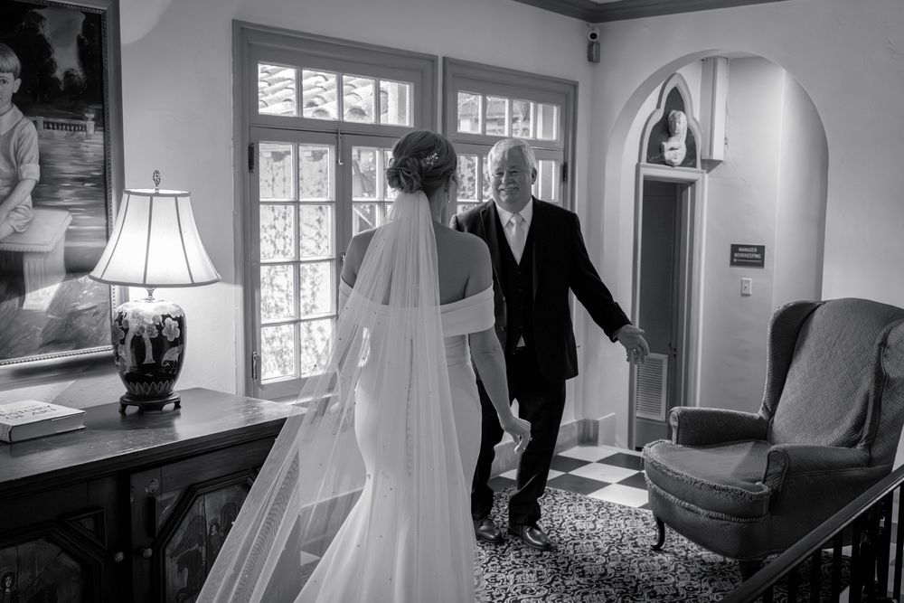 Black and white photo of a tender moment in an elegant room with large windows.