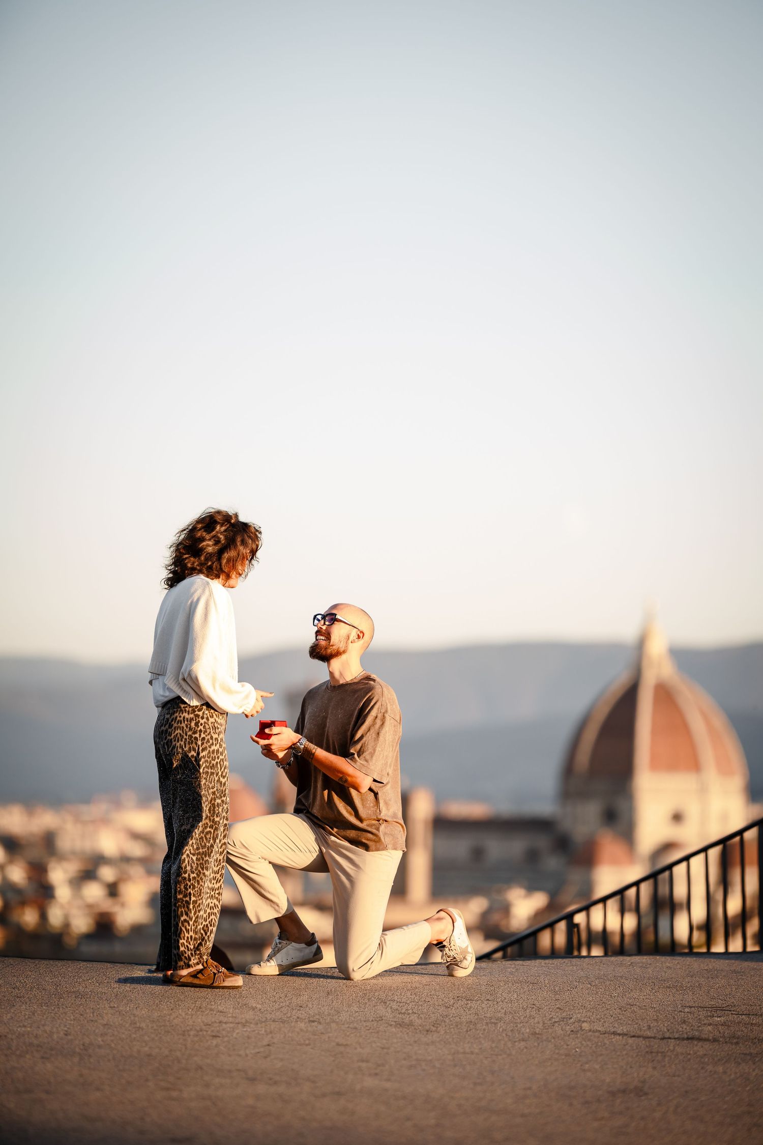 A romantic proposal moment unfolds on a scenic overlook with Florence's Duomo cathedral visible in the background.