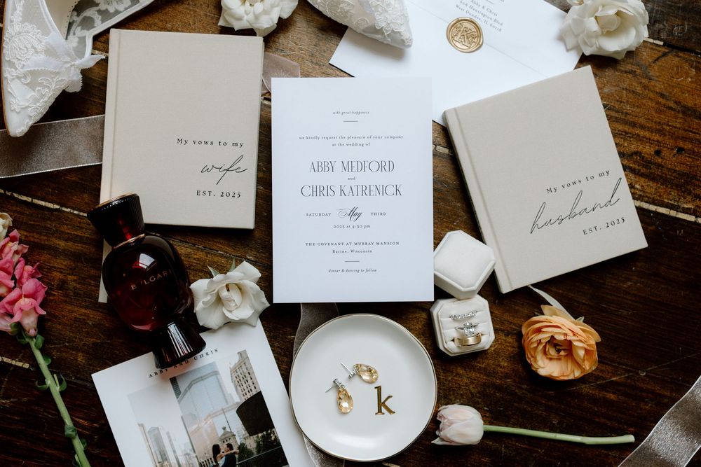 Elegant wedding stationery and invitations with white roses scattered on dark wooden table.