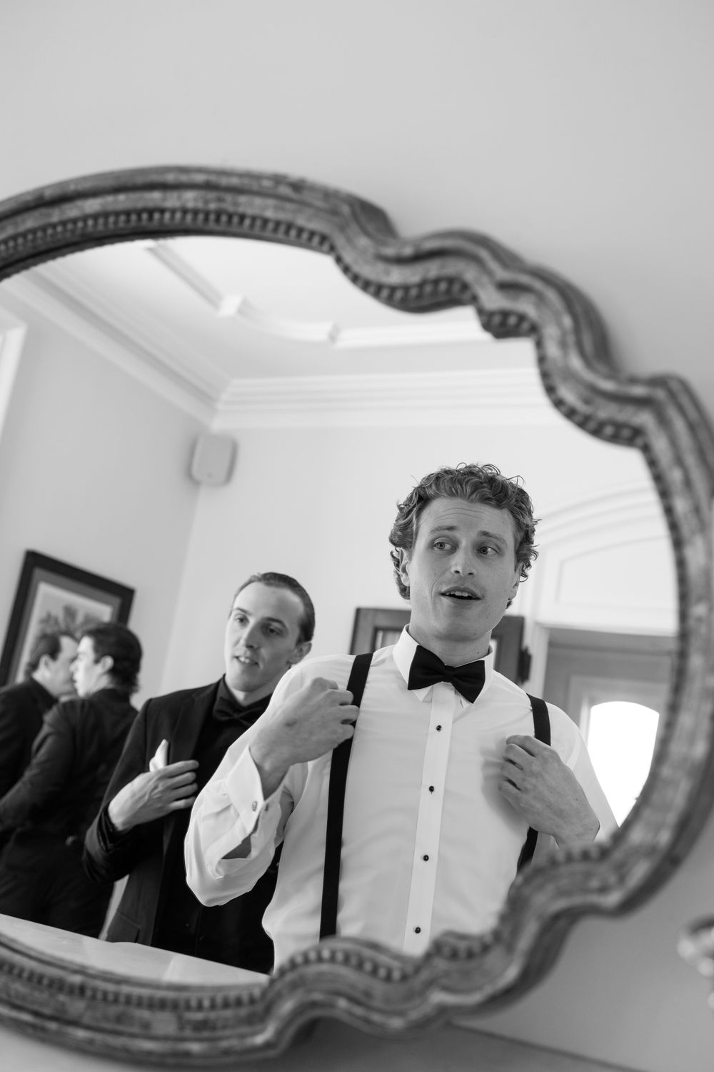 Black and white sequence of man adjusting bowtie in ornate mirror.