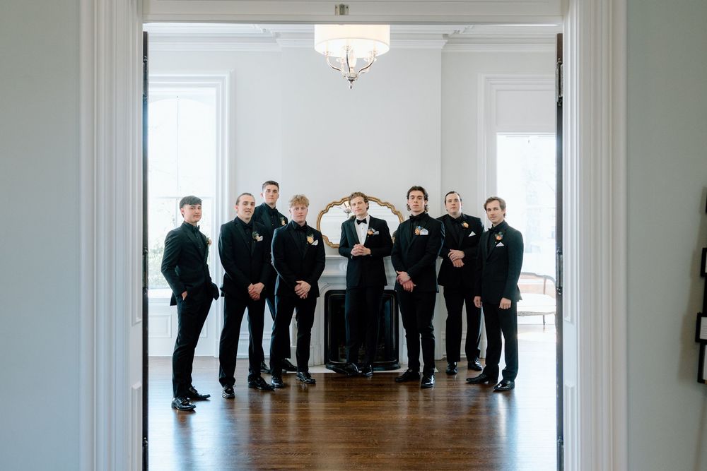 Wide angle view of wedding party in formal attire standing in bright white room.
