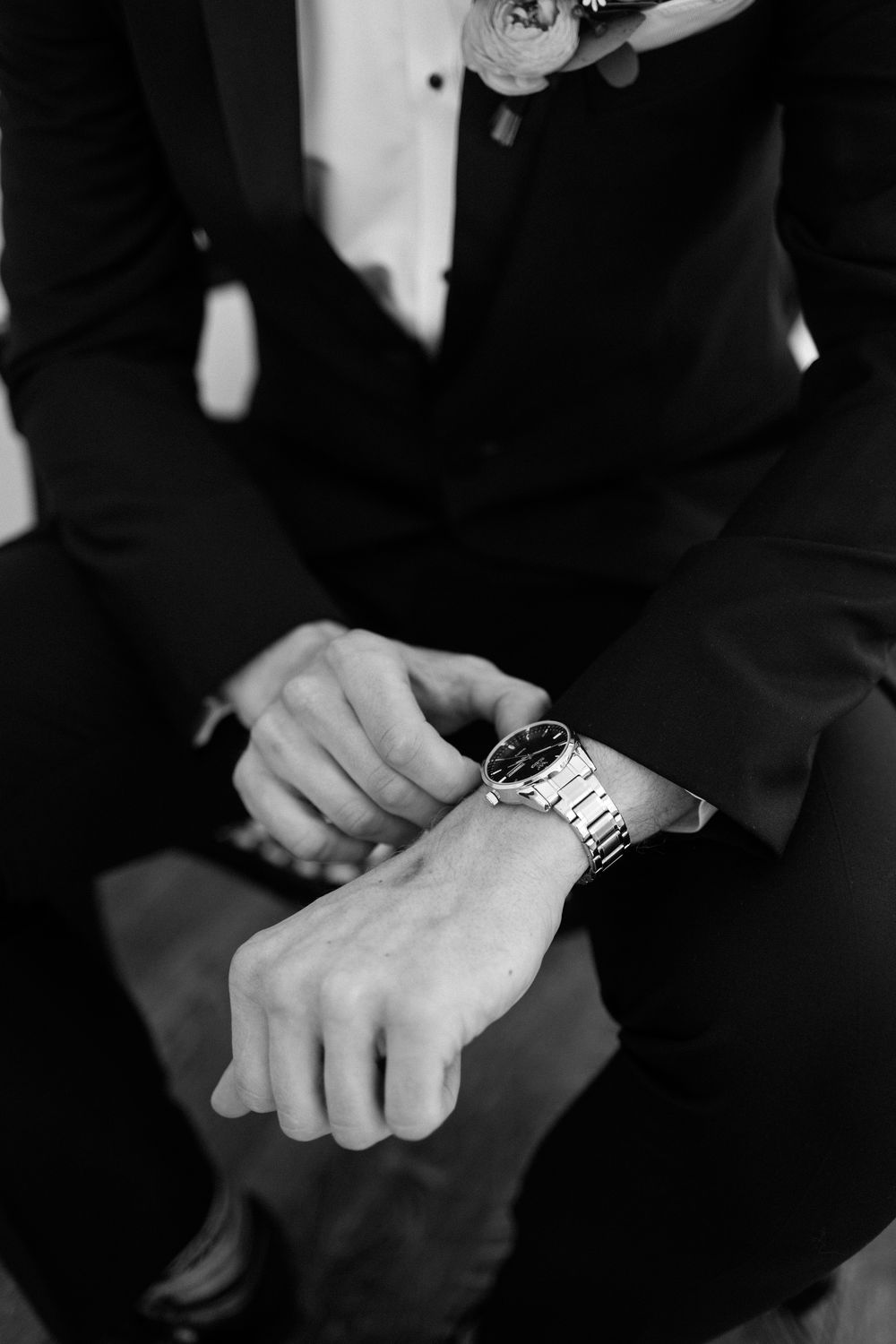 Black and white photo of someone in a suit checking their silver wristwatch.
