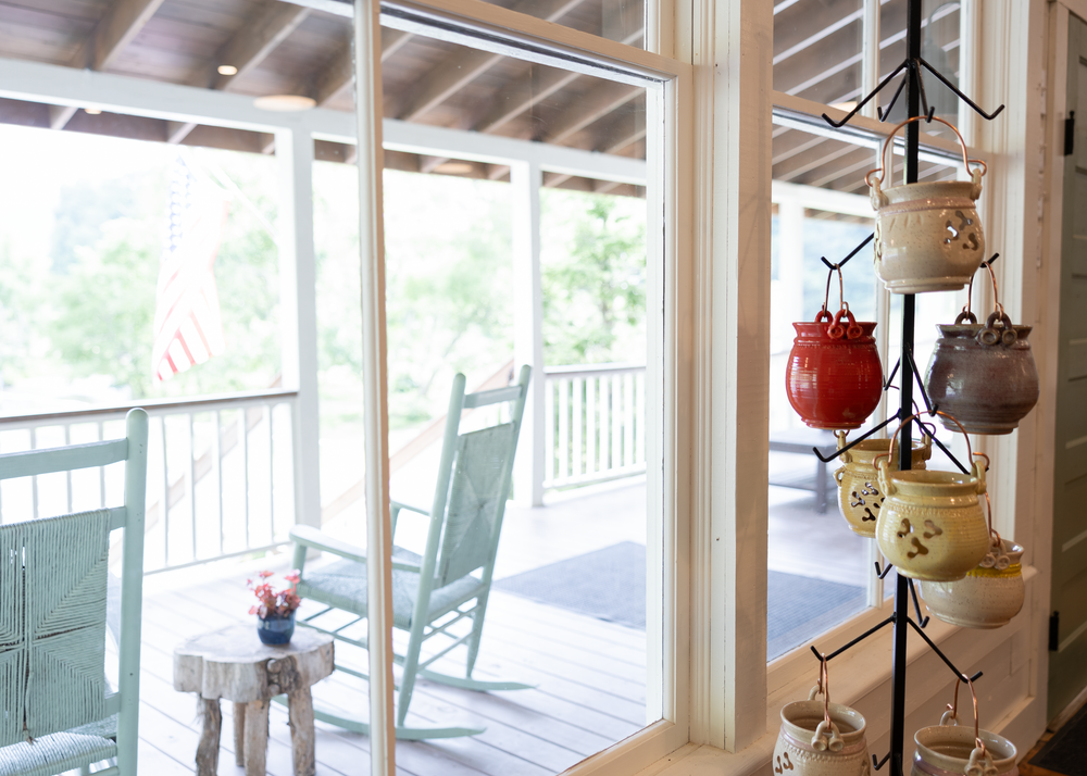 Screened porch with teal rocking chair, white side table, and hanging ceramic pottery display in a cozy cottage setting.