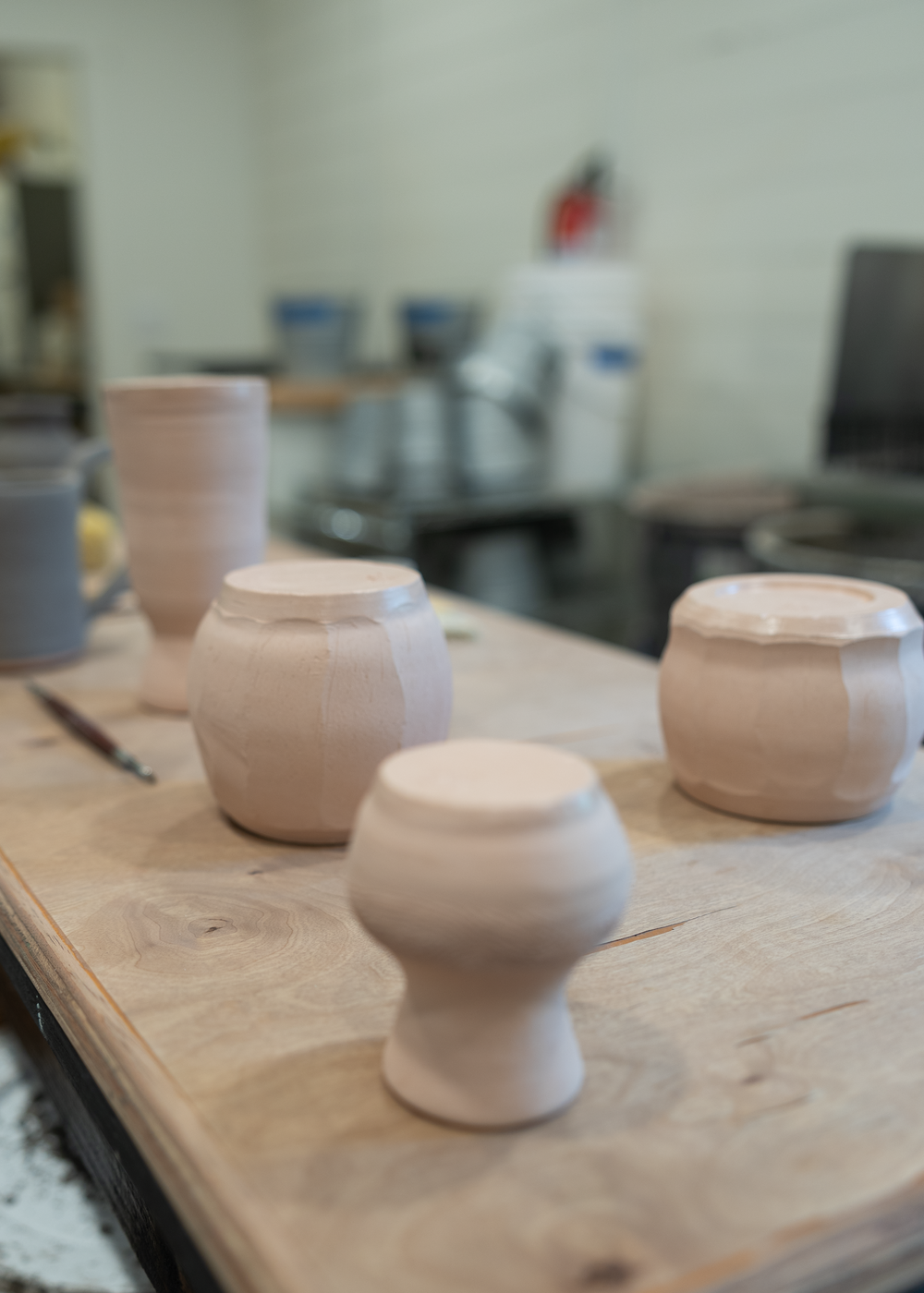 Four unfired white ceramic pottery pieces drying on a wooden workbench in a pottery studio.