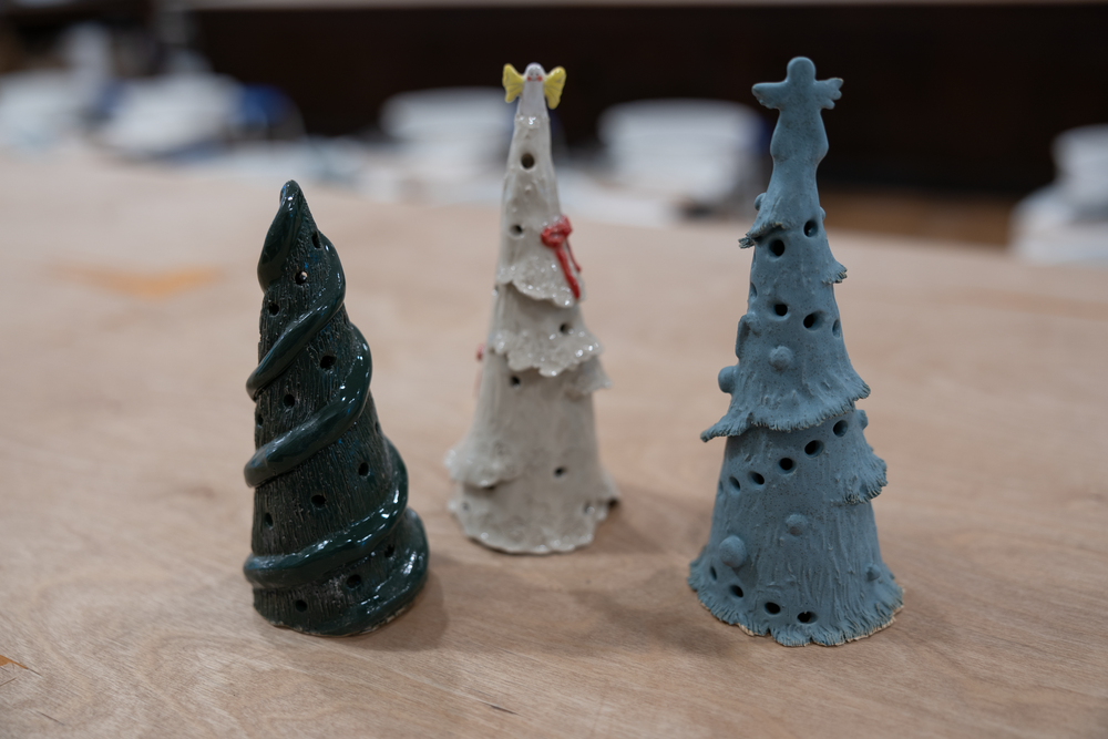 Three handmade ceramic Christmas tree sculptures in dark green, white, and light blue on a table.