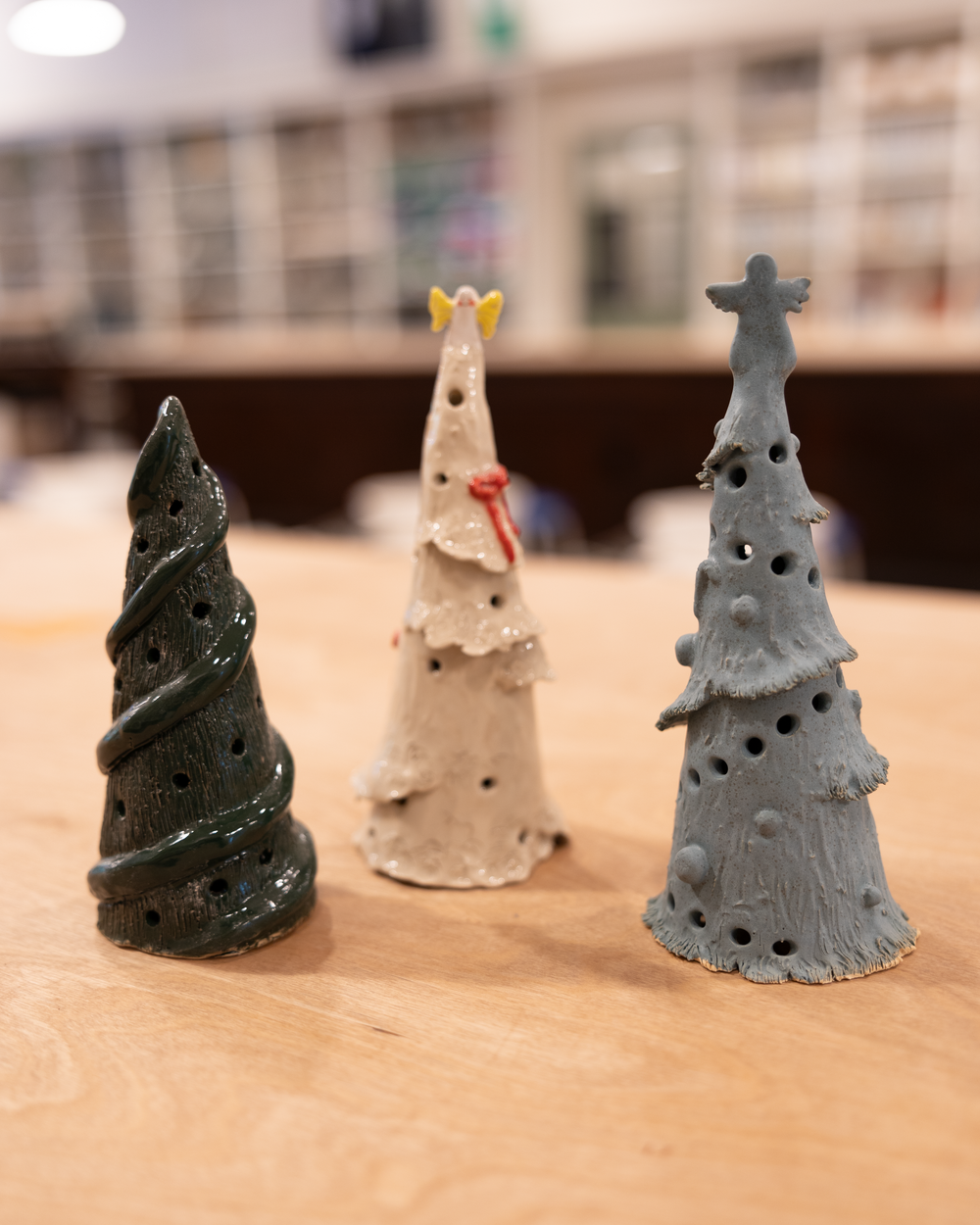 Three handmade ceramic Christmas tree figurines in green, white, and blue on a wooden table.