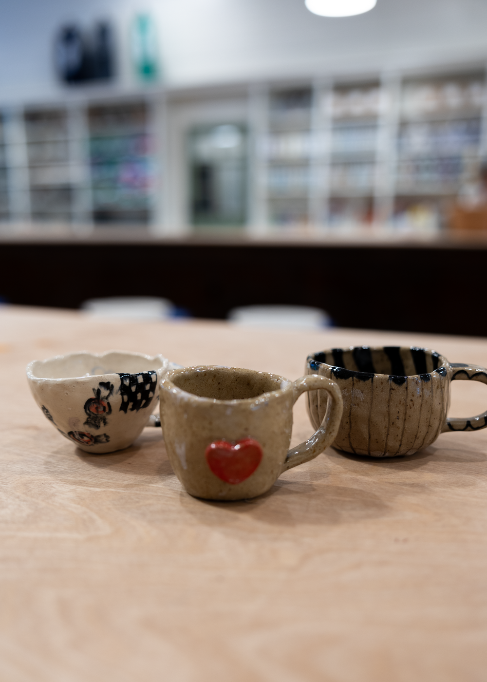 Three handmade ceramic mugs with decorative patterns including a red heart design on a wooden table.