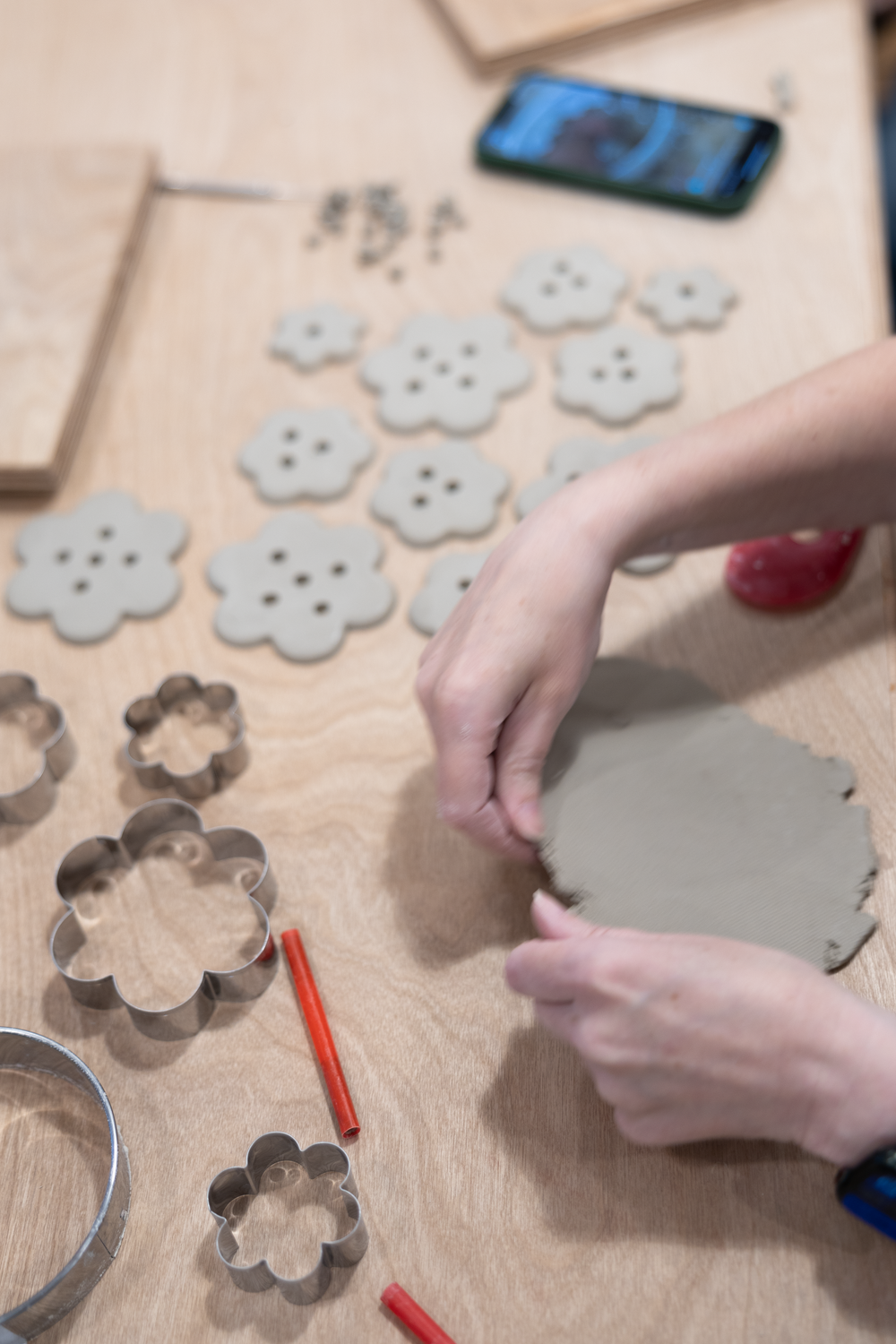 Hands shaping clay on wooden table with flower-shaped cookie cutters and clay pieces in pottery crafting workshop.