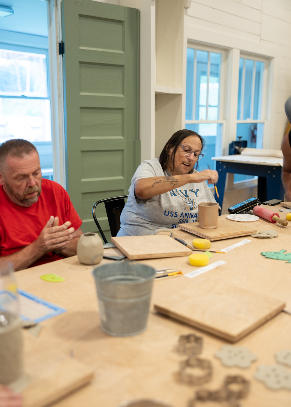 Adults engaged in a pottery clay crafting workshop, working at a wooden table in a bright studio.