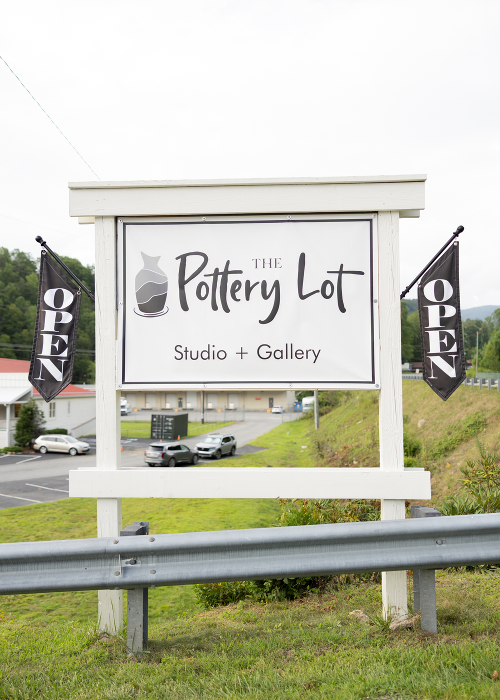 The Pottery Lot Studio and Gallery sign with open flags in a small town setting.