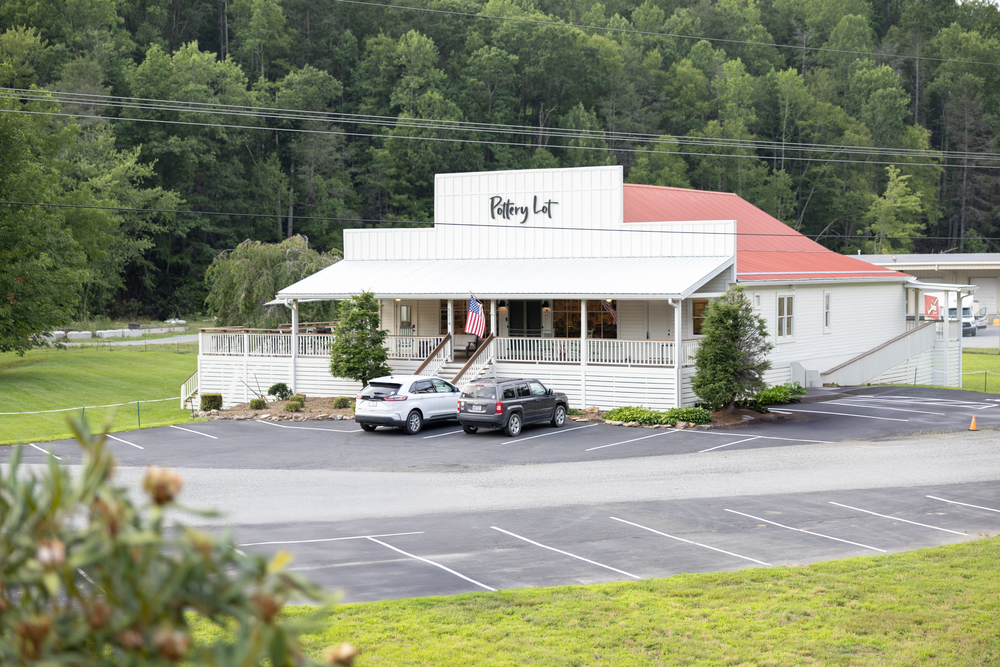 Riding Lot restaurant with covered porch, parking lot, and lush green forest backdrop in a rural setting.
