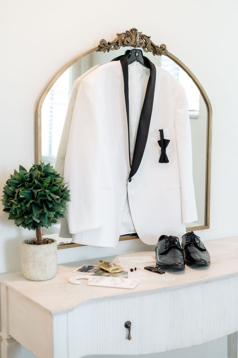 Wedding accessories including shoes, ties and decor arranged elegantly on white shelves with ornate gold mirrors.