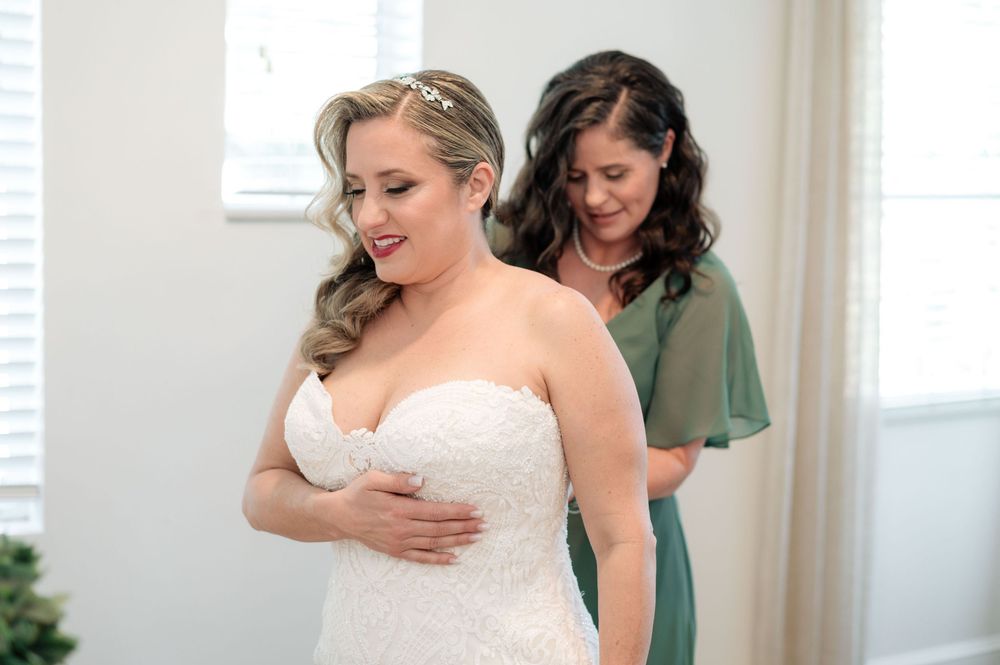 Bridal party in sage green dresses helps with wedding preparations in a bright indoor setting.