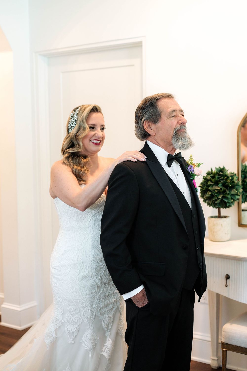 Candid first look moment between couple in formal wedding attire sharing laughter in white room.