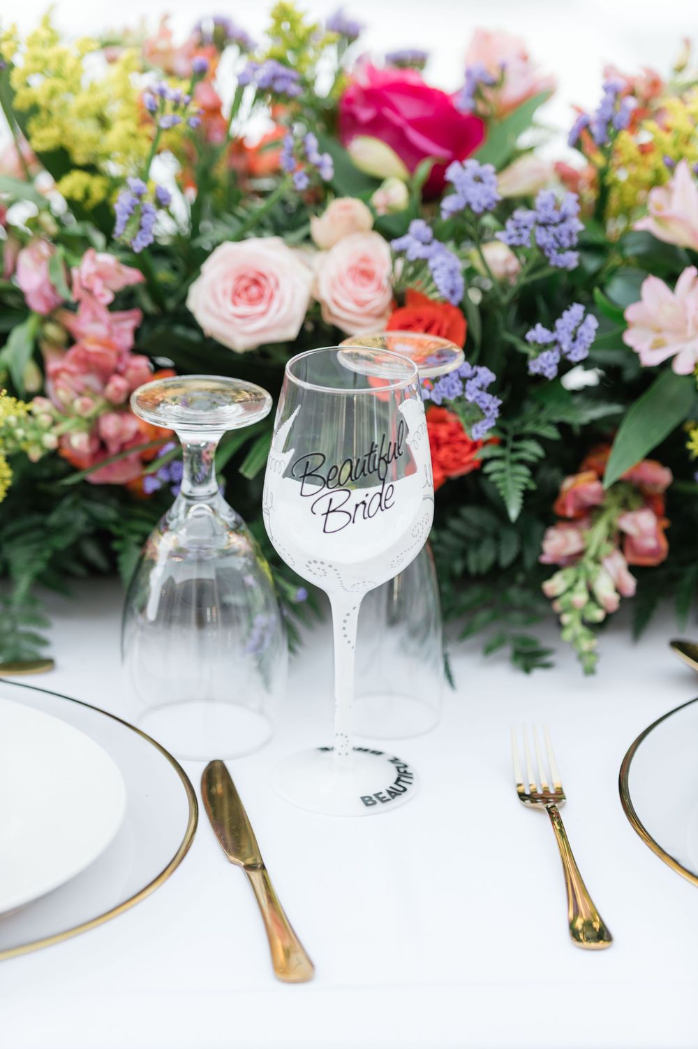 Colorful floral arrangements with pink roses and glassware set for an elegant wedding reception table.