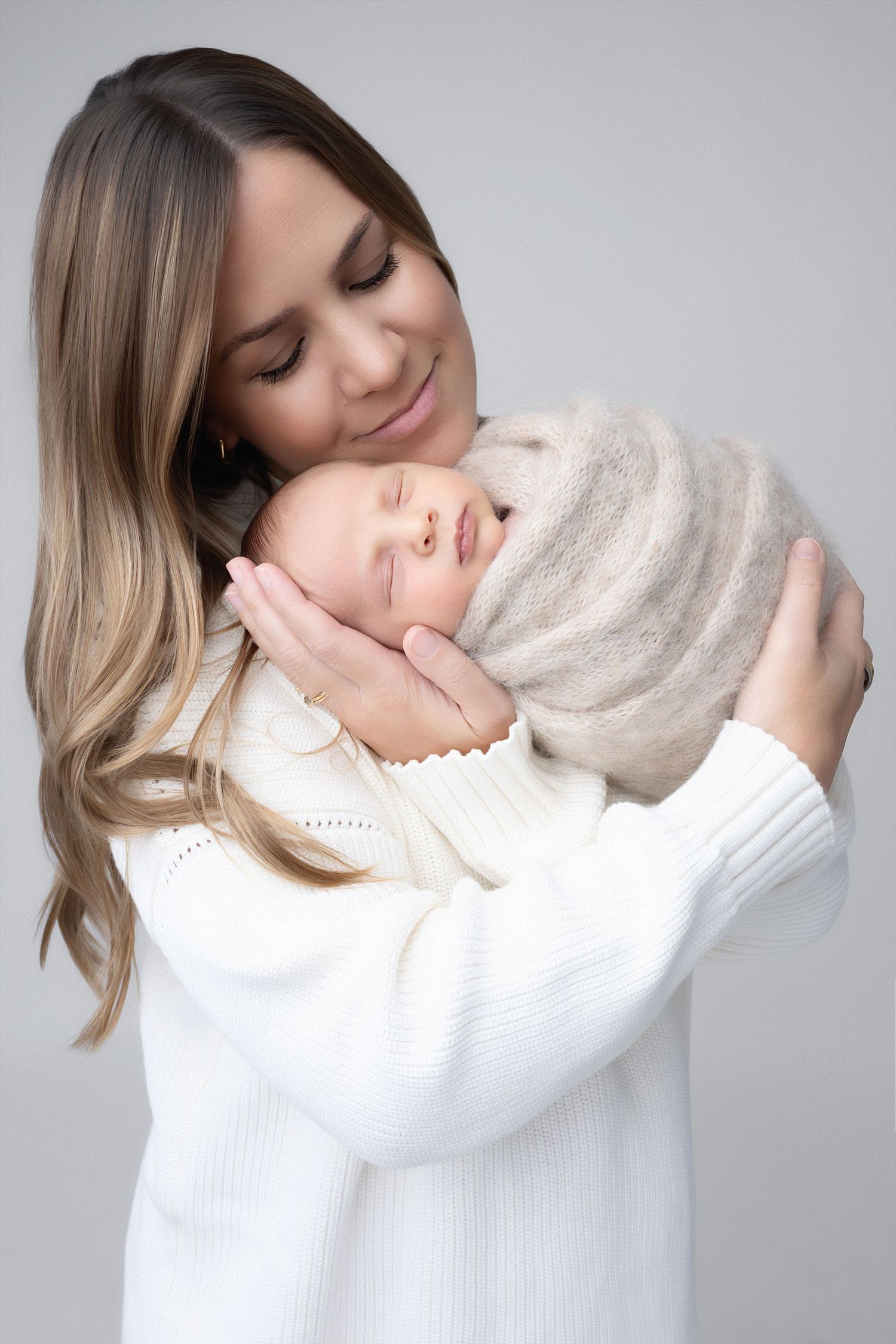 Series of photos showing a tender embrace between parent and baby in white sweaters against a light gray background.