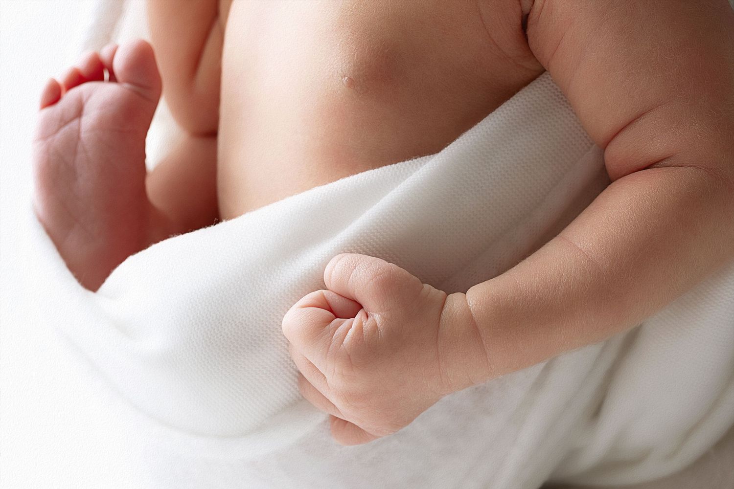 Close-up view of a newborn baby's tiny fingers wrapped around an adult's finger against a soft white background.