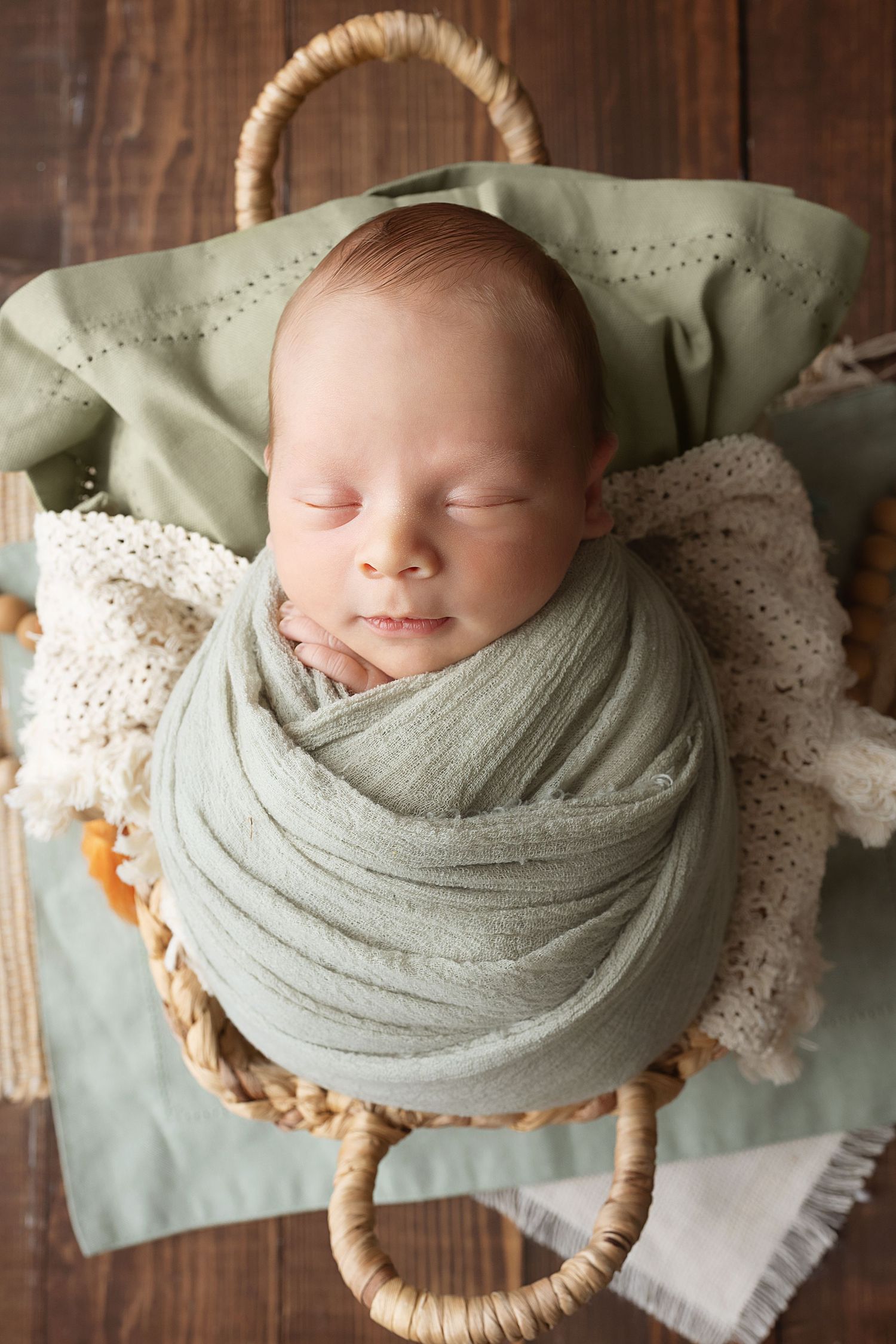 A sleeping newborn wrapped in soft gray fabric lies peacefully in a woven basket with lace accents.