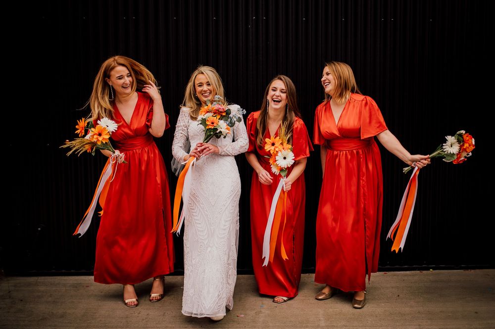 Bridesmaids in vibrant red dresses pose together with a bride in white during a wedding photo session.