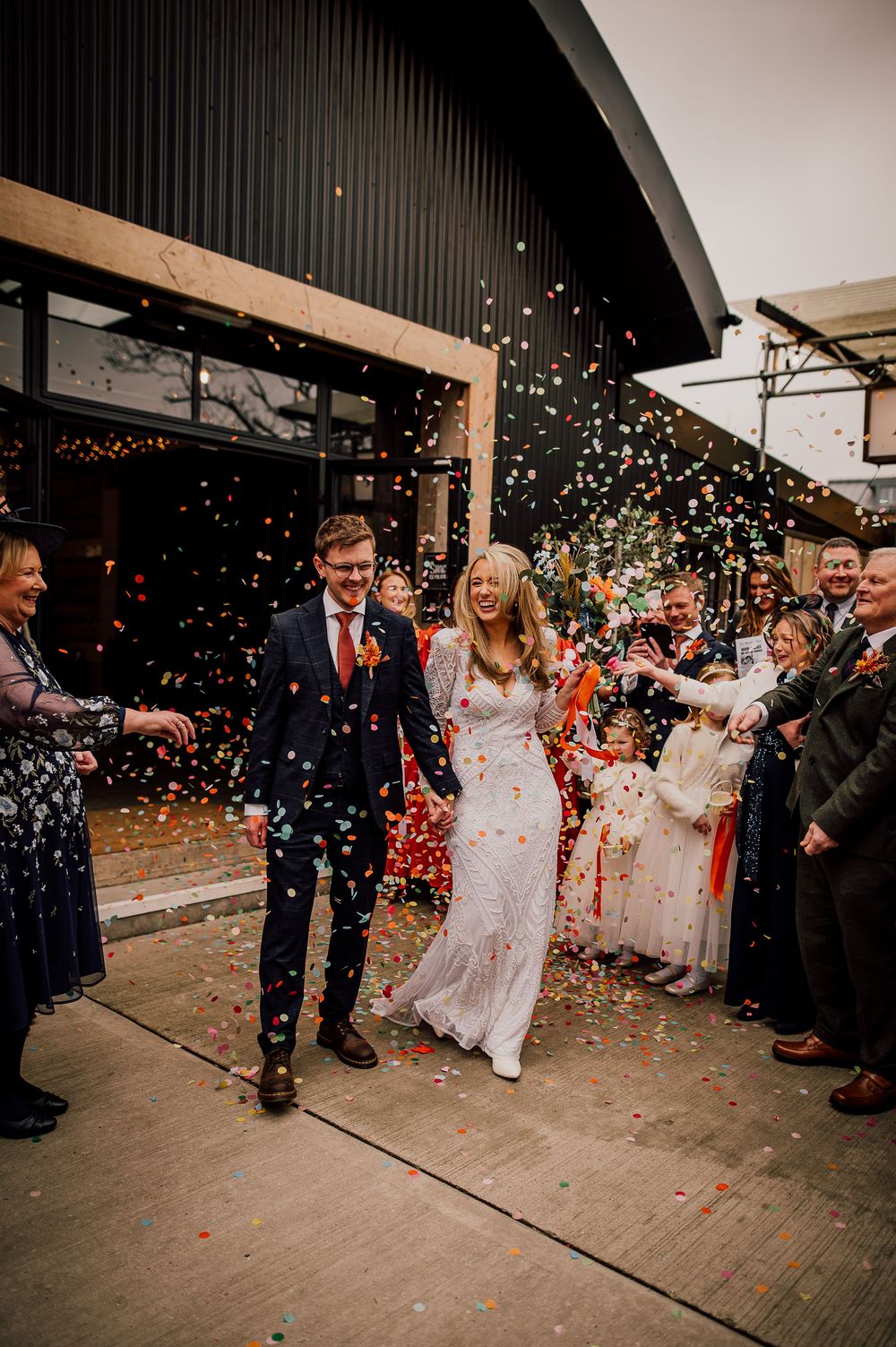 Wedding guests shower the newlyweds with colorful confetti during their joyous exit celebration at a rustic venue.