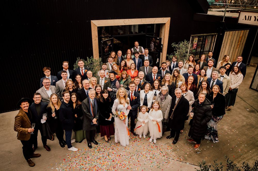 Wedding guests pose together in a panoramic sequence of group photos at an outdoor venue.