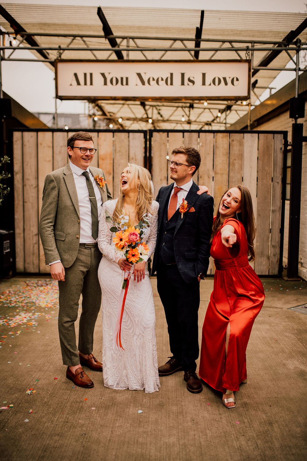Wedding party laughs and poses together in an industrial venue with warm lighting and rustic wooden walls.