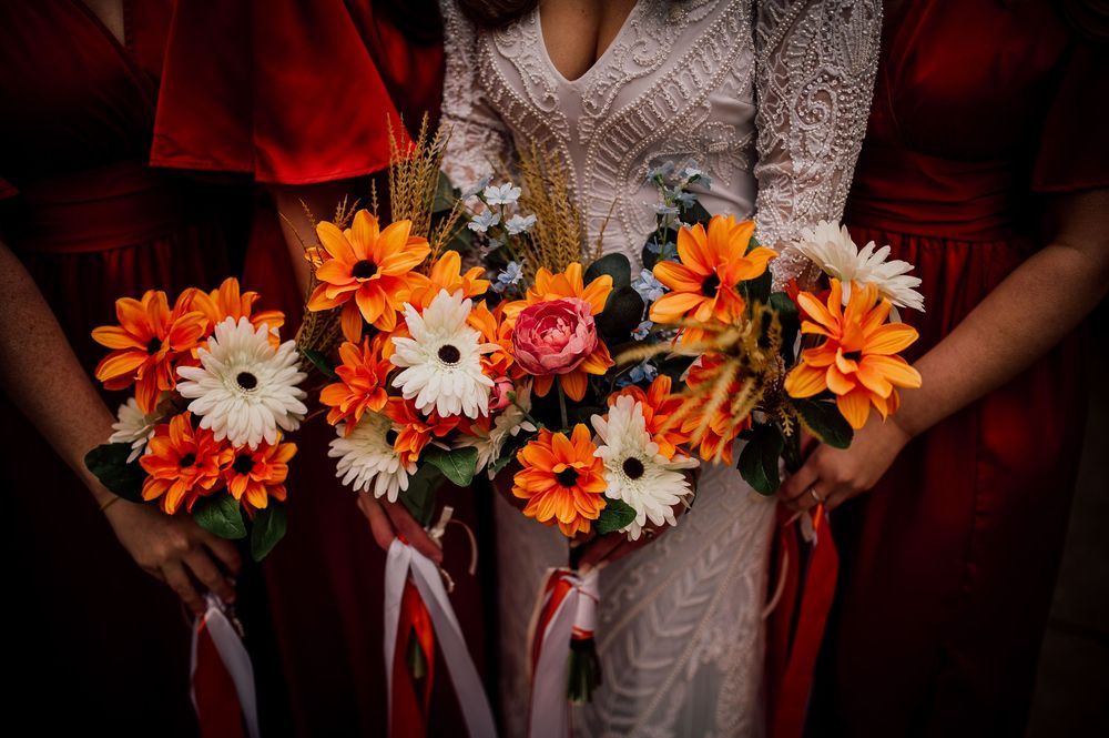 Wedding bouquets with orange and white daisies arranged in a row with red ribbons and decorative accents.