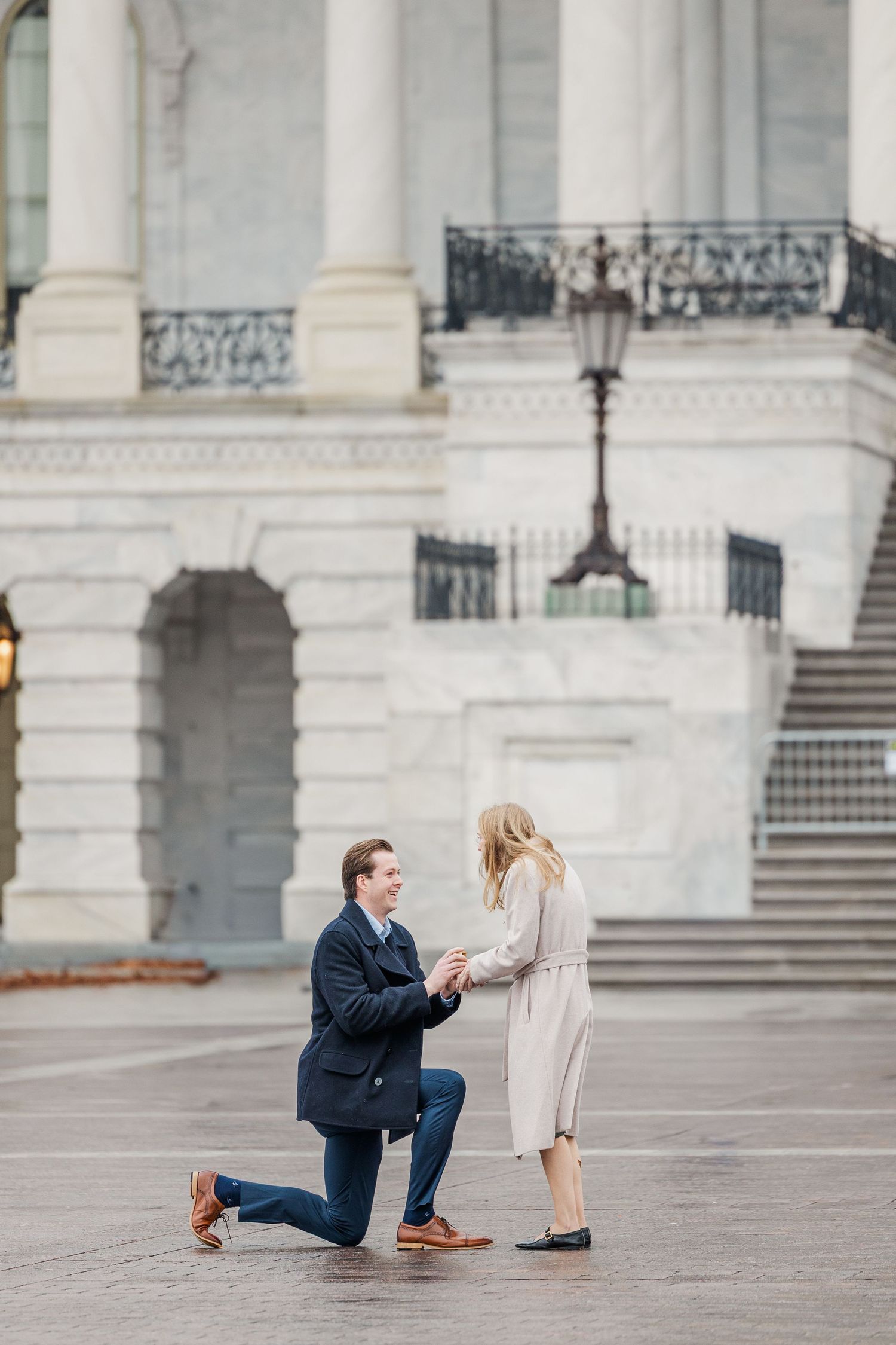 A romantic proposal moment unfolds on the steps of a grand government building with white columns and architecture.