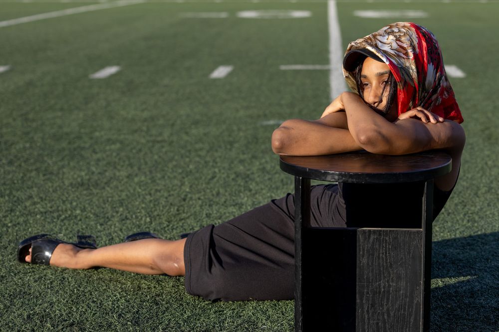 Person in athletic wear rests on a bench at a football field with yard line markers visible.