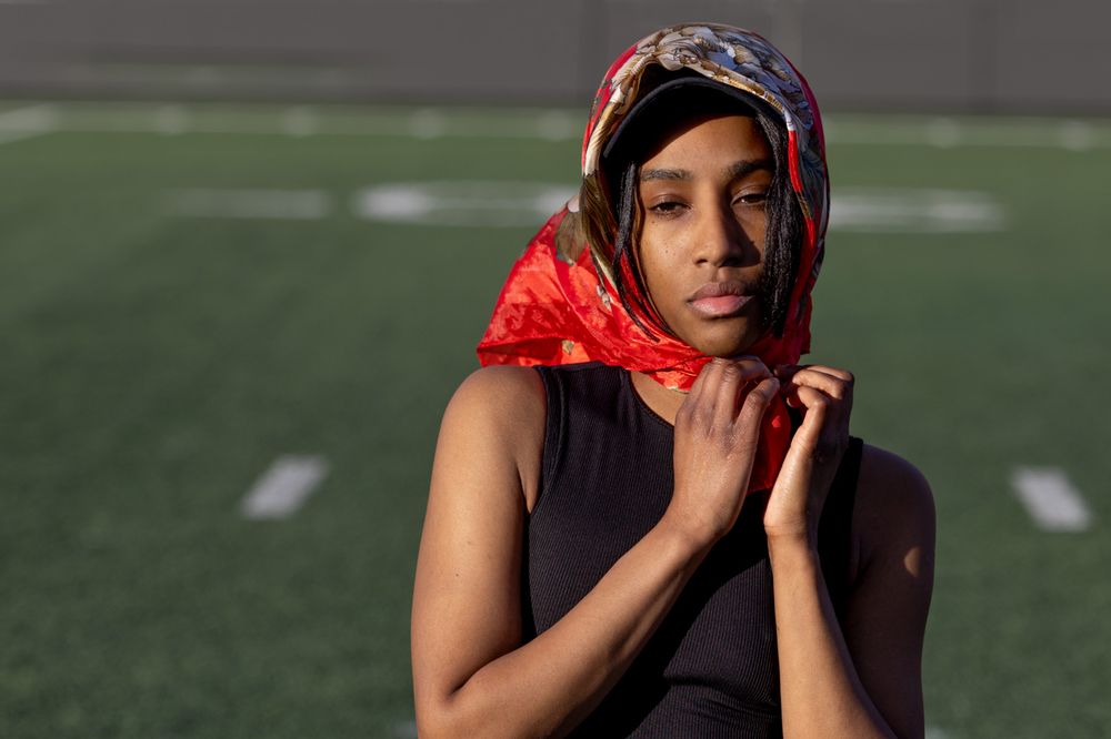 Athletic figure in red and black workout attire sits thoughtfully on a sports field during golden hour.