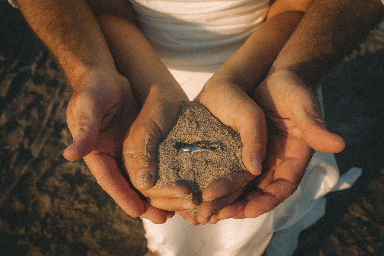 Elopement wedding rings holding in hands full of sand