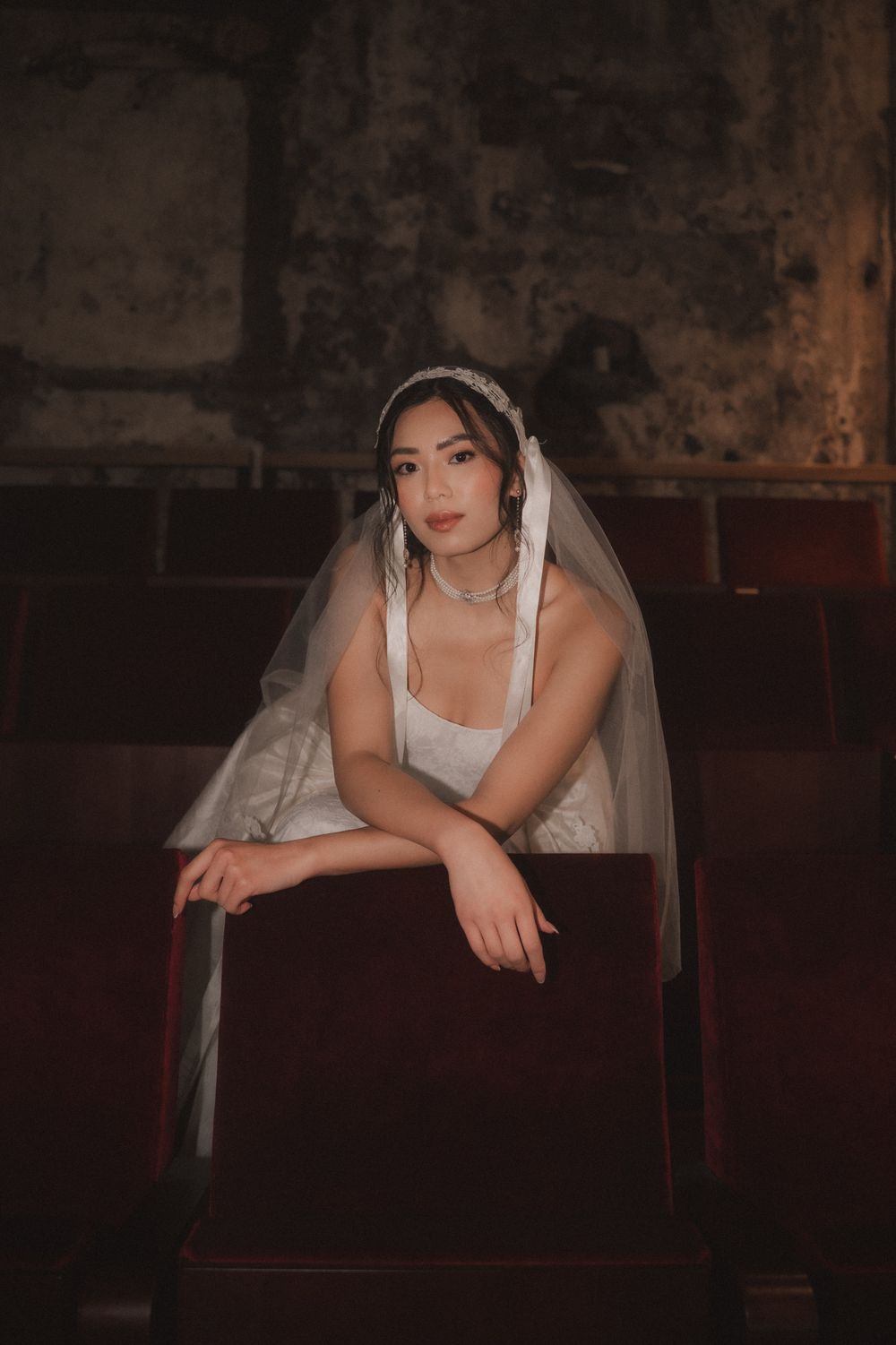 A bride in a white wedding dress leans on a dark wooden pew in a dimly lit church interior.