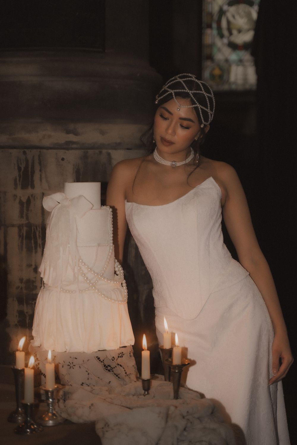 A moody portrait setup with white candles and elegant white dress against a dark, atmospheric background.