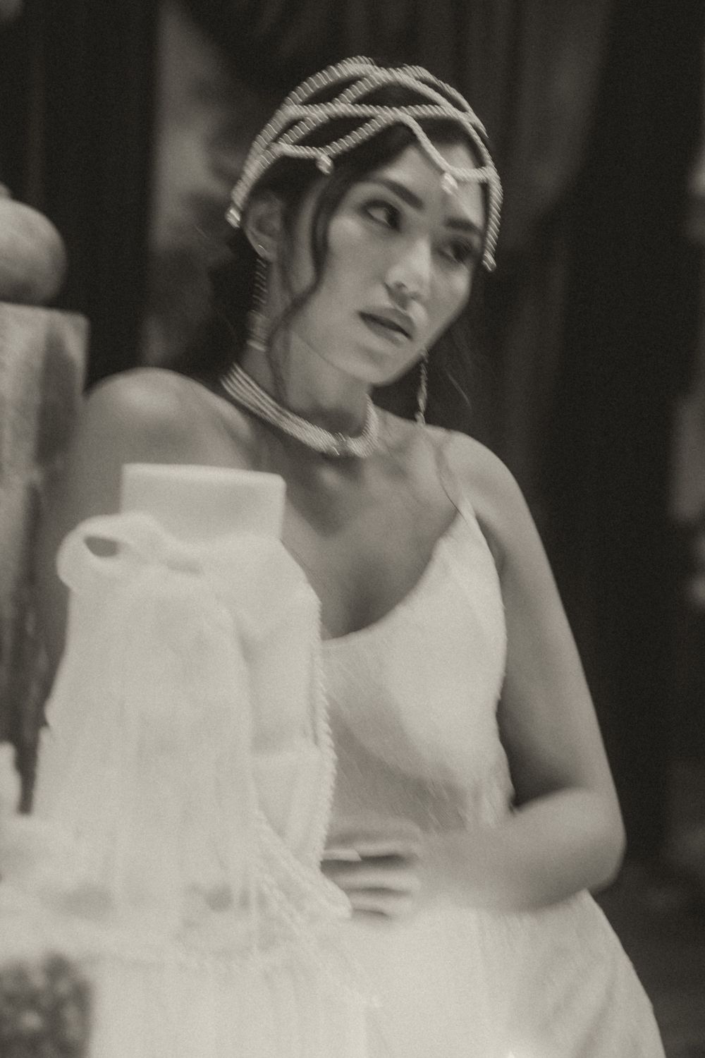 Black and white vintage portrait of a woman in a white dress and striped headpiece looking to the side.