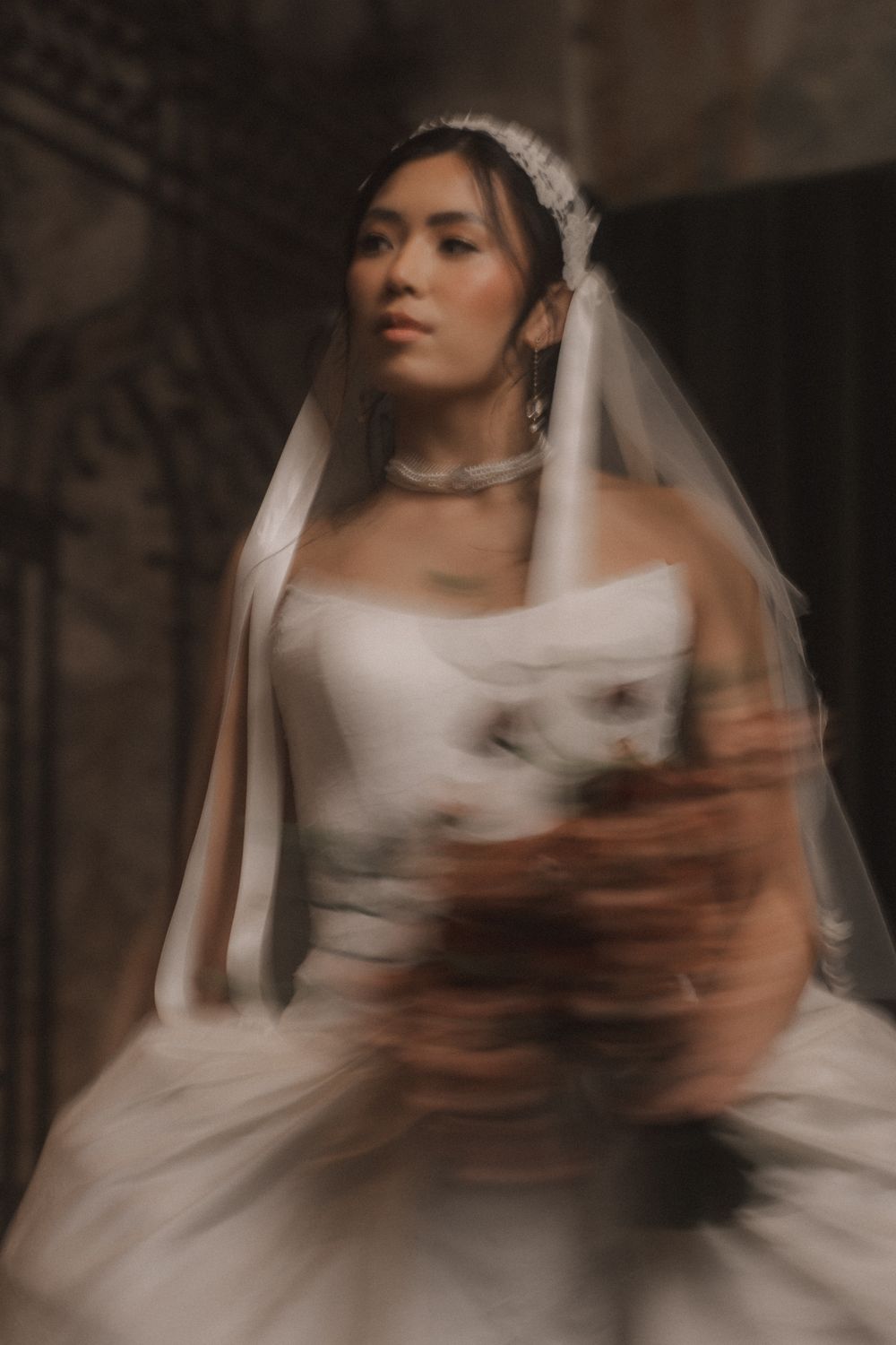Artistic motion-blur wedding portrait shows bride in white gown and veil with dreamy ethereal lighting effect.