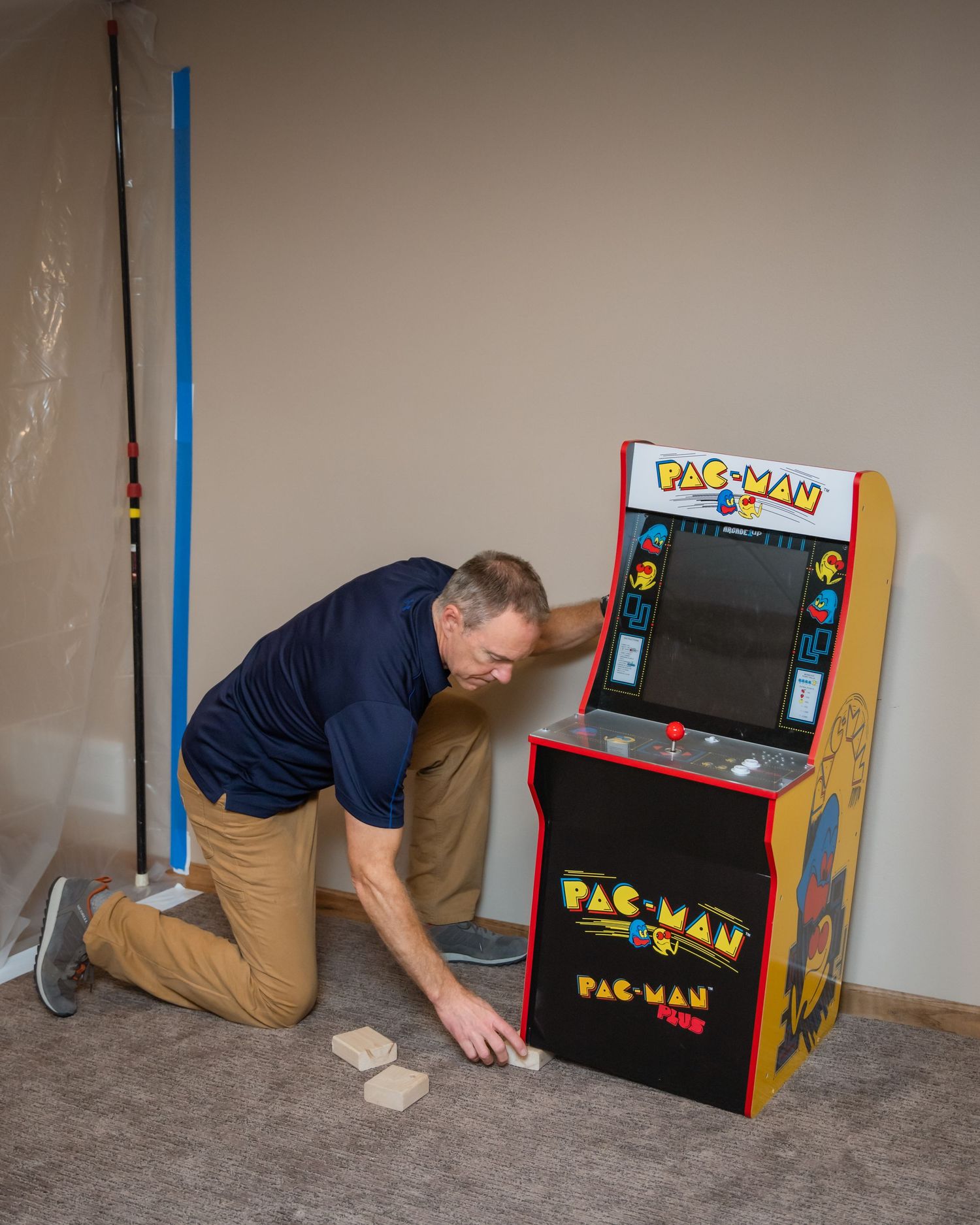 A series of images showing someone assembling a retro Pac-Man arcade cabinet on a carpeted floor.