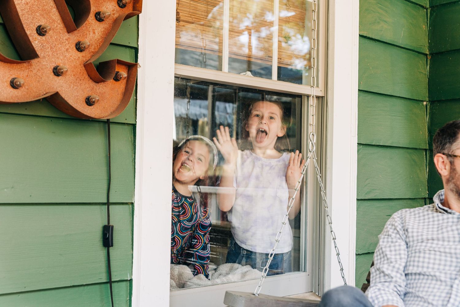 Green house with a window where two young sisters are making silly faces from inside the house in Charlotte, NC.