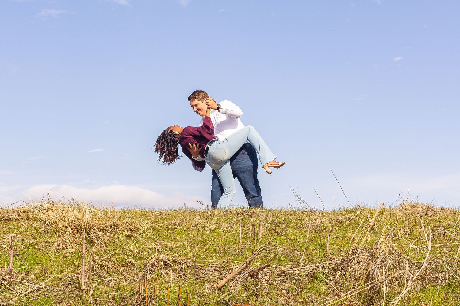 A couple dances with a bright blue background in a grassy field.