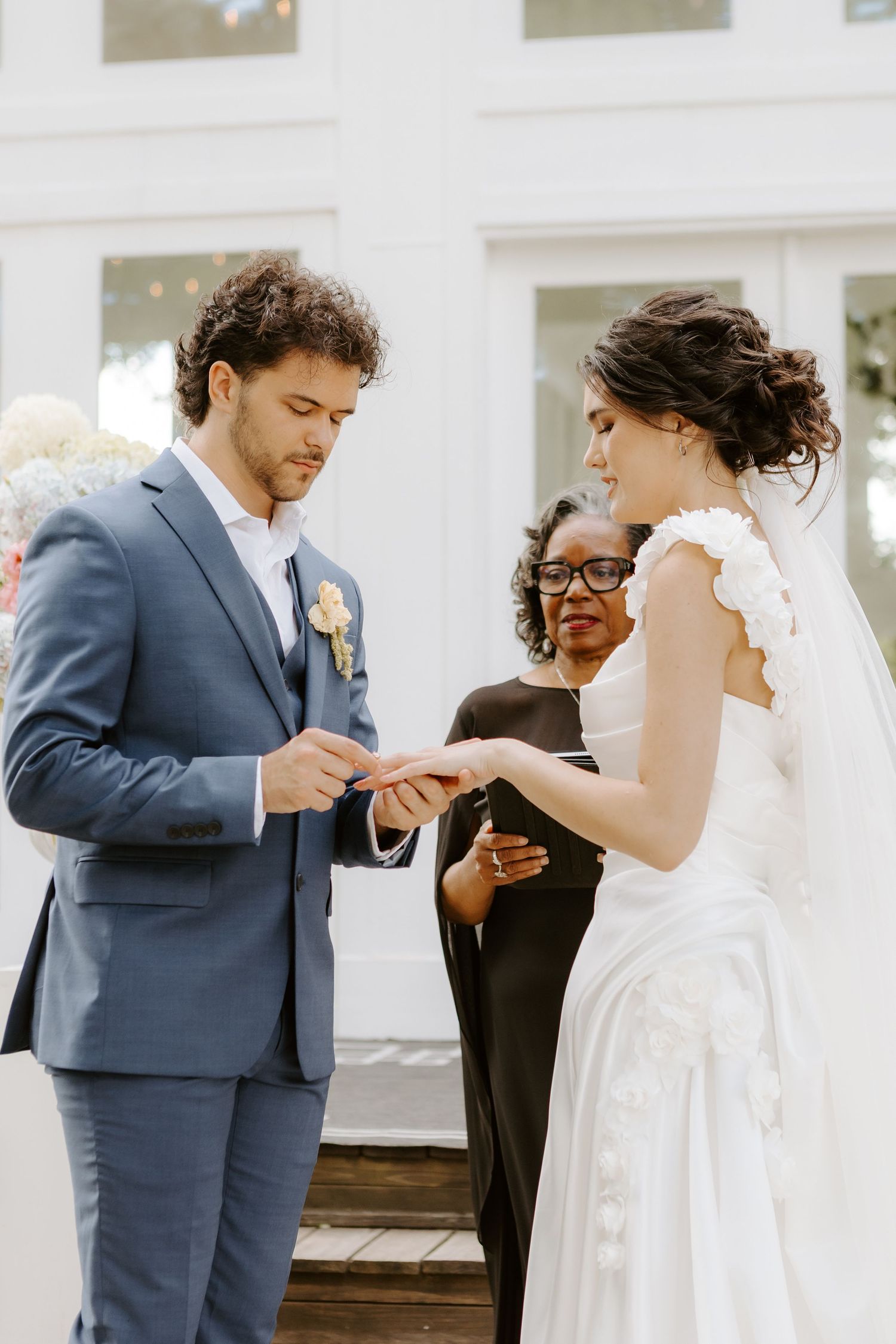 Bride in off-shoulder white gown and groom in tan suit holding hands walking in meadow.
