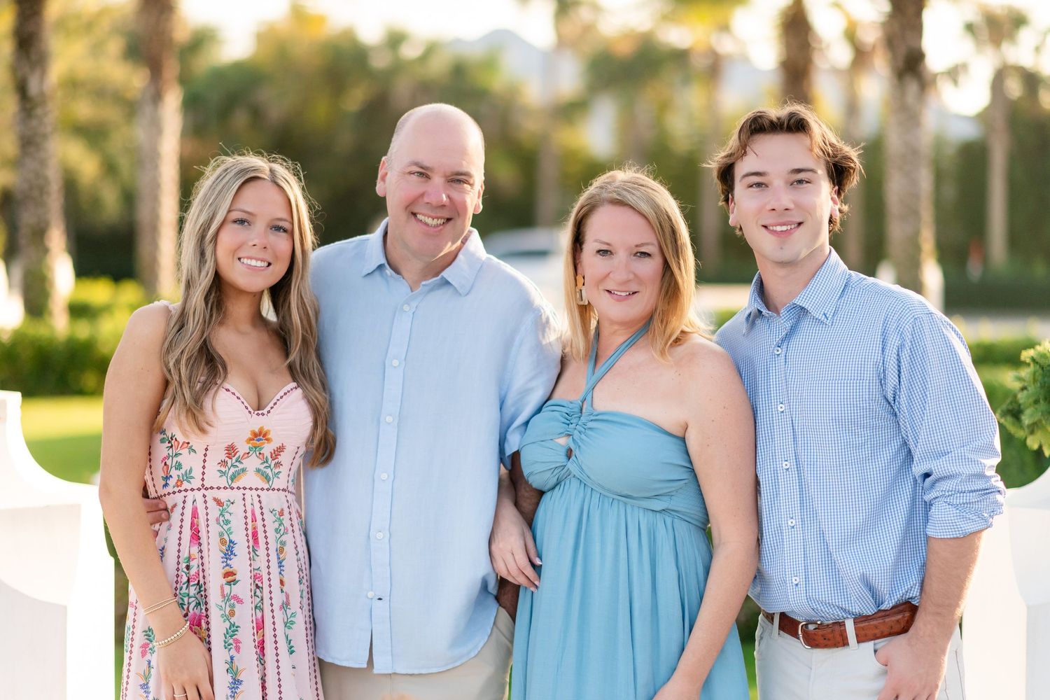 A family group wearing coordinated blue and white outfits poses together outdoors during a sunset photo session.